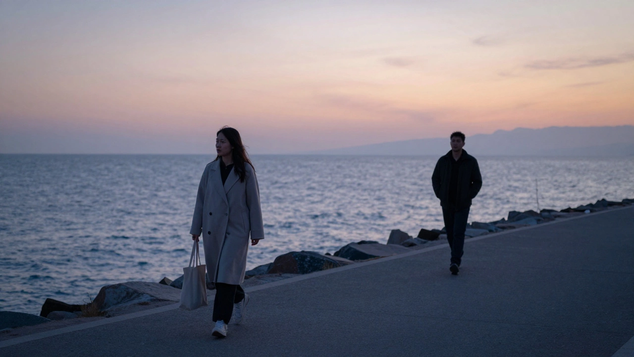 A couple walks along a quiet coastal path at dusk, the sea glowing behind them under a soft twilight sky.